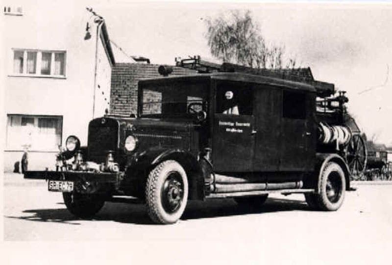 Schwarz-Weiß-Foto eines frühen Feuerwehr-Löschfahrzeugs vor einem Gebäude in Straßkirchen